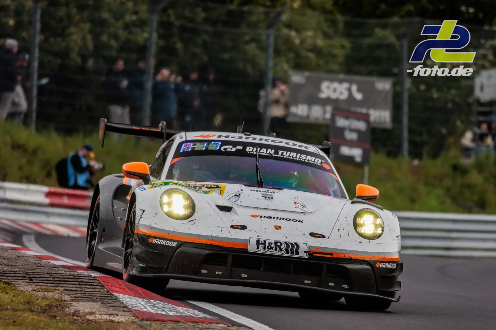 Porsche 911 GT3 R mit weißer Lackierung und orangen Details auf der Nürburgring-Nordschleife während des 24-Stunden-Rennens.