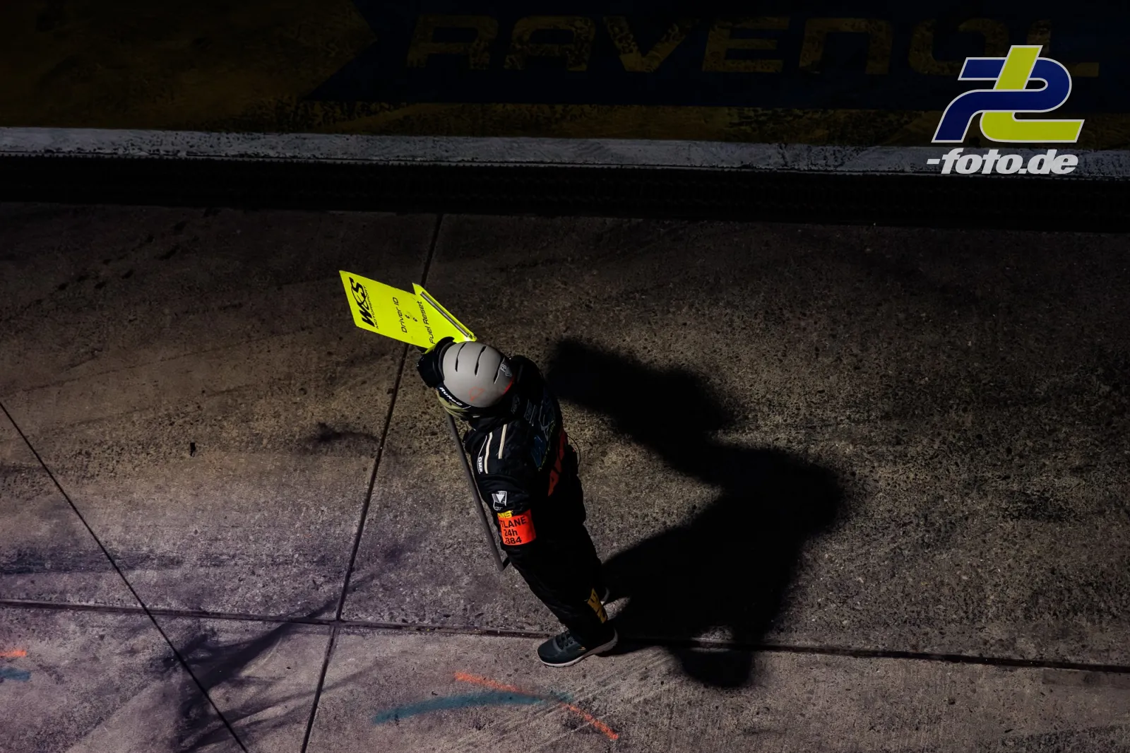 Streckenposten mit gelber Flagge auf dem Asphalt während des ADAC RAVENOL 24h Nürburgring, Vogelperspektive mit Schatten.