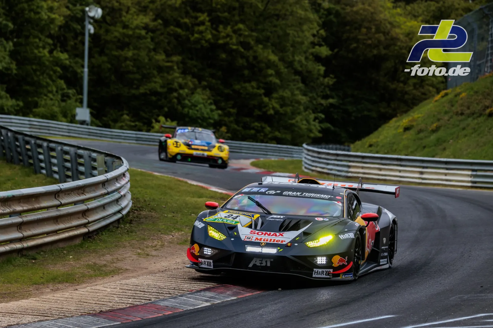 Lamborghini Huracán GT3 EVO2 durchfährt Kurve auf der Nordschleife, gelb-schwarzes Fahrzeug im Hintergrund.
