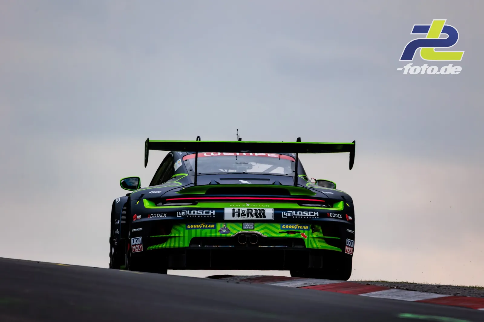 Porsche 911 GT3 R in schwarz-grüner Lackierung von hinten auf Bergkuppe, 24h Nürburgring
