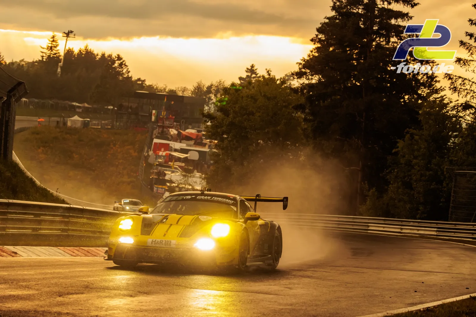 Gelber Rennwagen mit Licht bei Sonnenuntergang auf nasser Strecke am Nürburgring, dahinter weitere Fahrzeuge im Gegenlicht.
