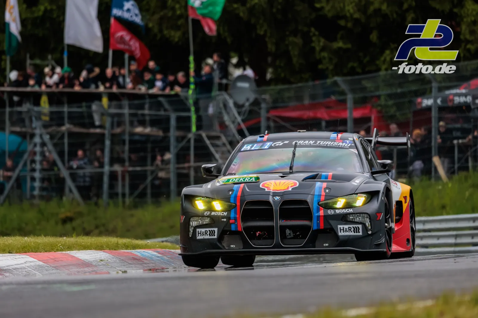 BMW M4 GT3 in grauer Shell-Lackierung in einer Kurve auf dem Nürburgring vor Zuschauertribüne beim 24-Stunden-Rennen.