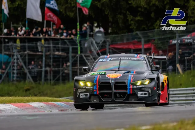 BMW M4 GT3 in grauer Shell-Lackierung in einer Kurve auf dem Nürburgring vor Zuschauertribüne beim 24-Stunden-Rennen.
