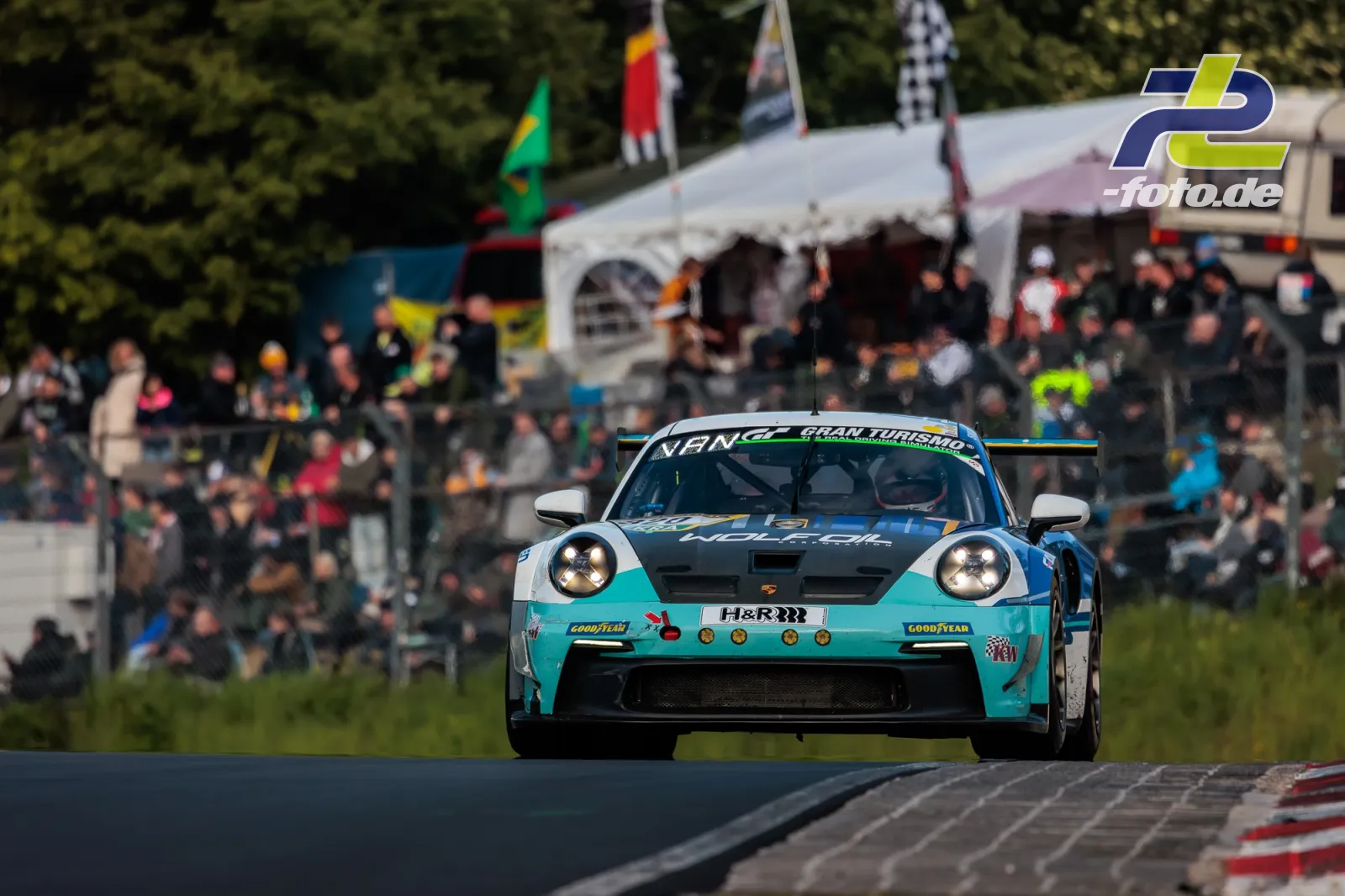 Porsche 911 GT3 in türkisblauer Lackierung vor Zuschauerbereich bei den 24h Nürburgring, Frontansicht in Kurve