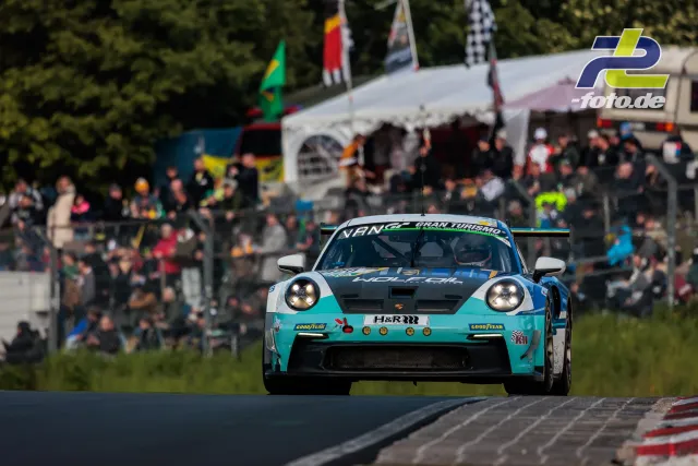 Porsche 911 GT3 in türkisblauer Lackierung vor Zuschauerbereich bei den 24h Nürburgring, Frontansicht in Kurve