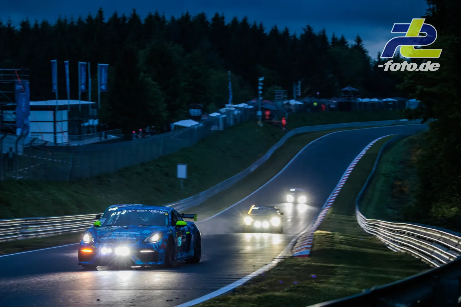 Porsche 718 Cayman GT4 Clubsport #82 fährt bei Dämmerung mit eingeschalteten Scheinwerfern durch eine Kurve der Nürburgring-Nordschleife.
