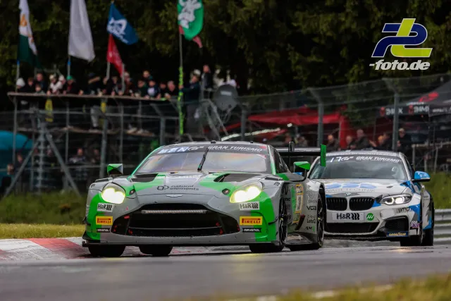 Zweikampf zwischen Aston Martin Vantage GT3 und BMW M4 GT3 im Rennen beim 24h-Rennen Nürburgring mit Zuschauern im Hintergrund