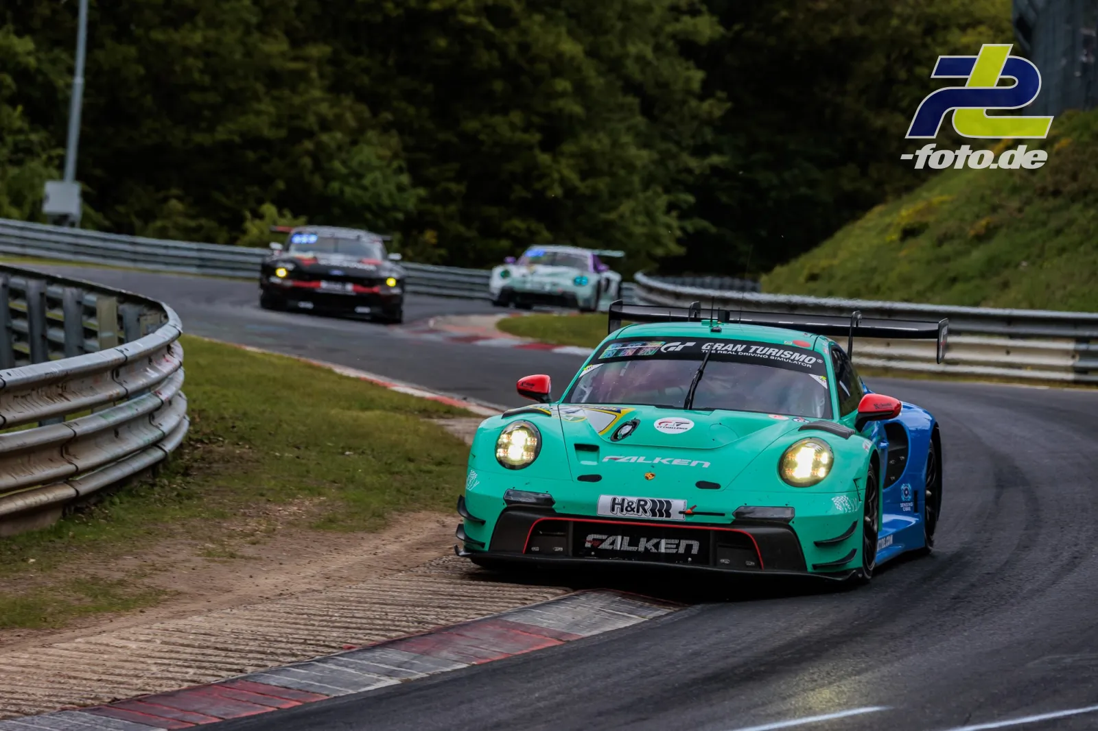 Türkiser Porsche 911 GT3 R in Kurve auf der Nordschleife, gefolgt von zwei weiteren Fahrzeugen während des 24h-Rennens
