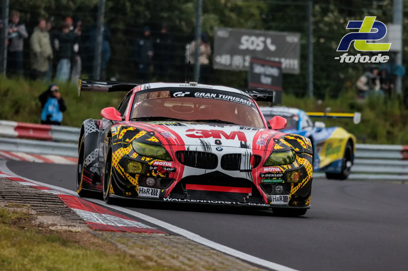 BMW E89 Z4 von Walkenhorst Motorsport in rot-weißer Lackierung auf dem Nürburgring beim 24h-Rennen, Kurvenfahrt mit Zuschauern im Hintergrund.