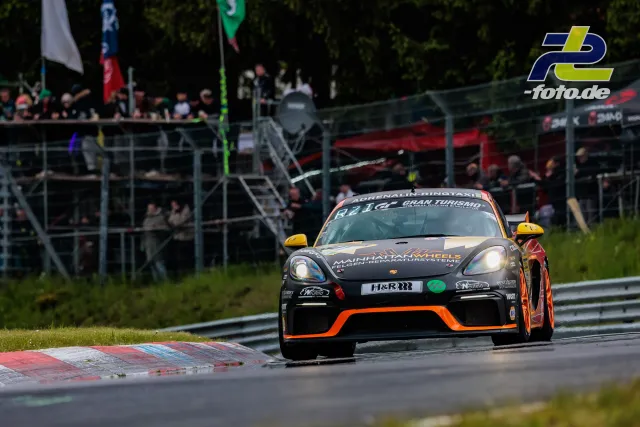 Porsche Cayman GT4 auf der Nordschleife beim 24h-Rennen Nürburgring, Zuschauertribüne im Hintergrund.