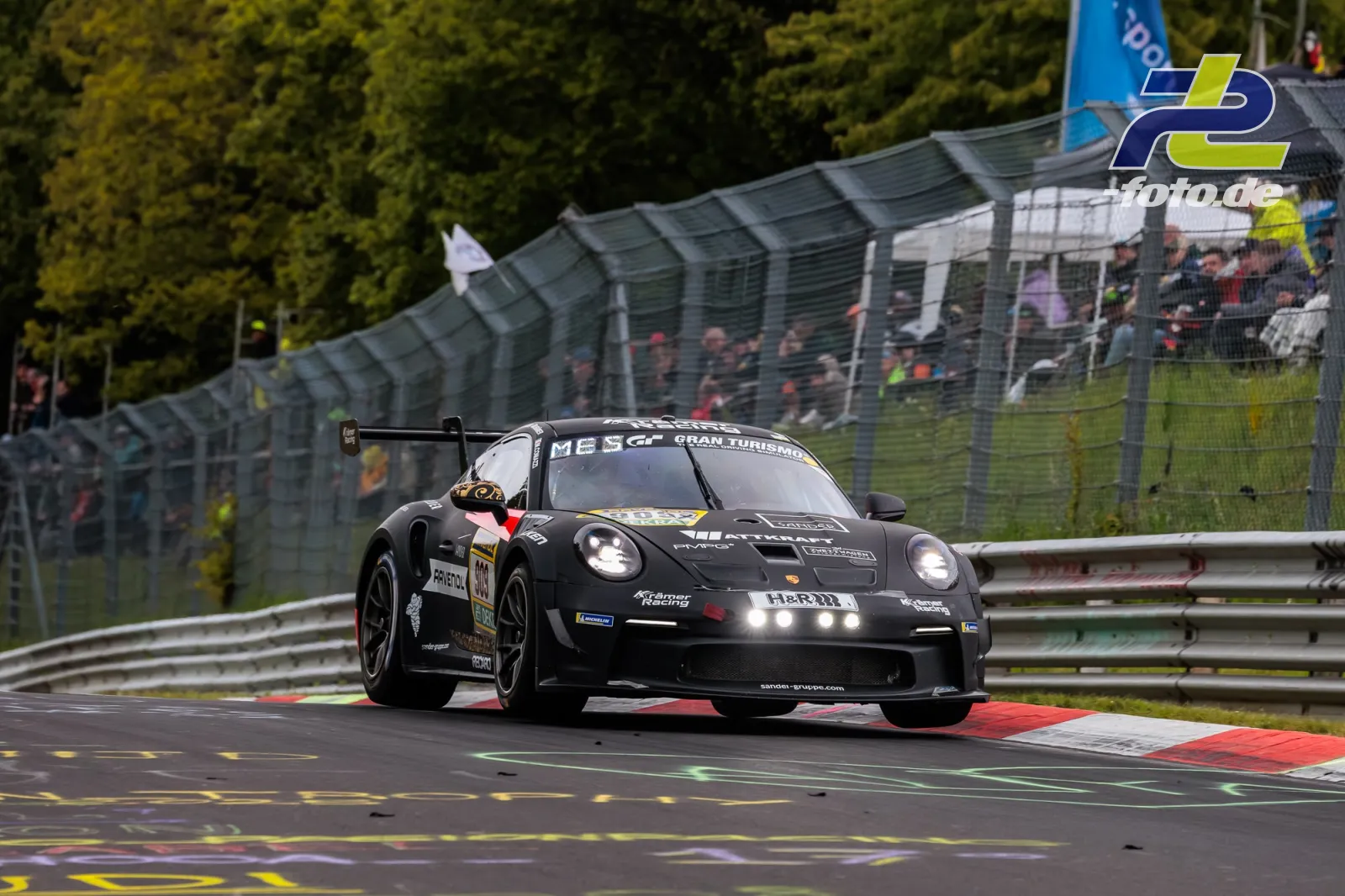 Schwarzer Porsche 911 GT3 Cup (992) #909 von KKrämer Racing fährt über Randstein auf nasser Strecke beim 24h-Rennen Nürburgring.