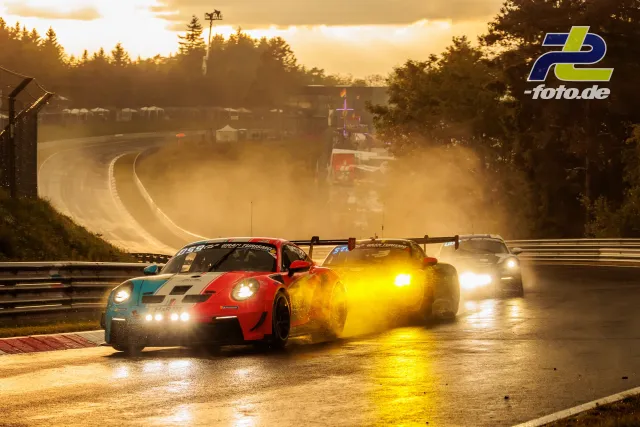 Drei GT-Fahrzeuge auf nasser Nordschleife bei Gegenlicht und dramatischer Abendsonne mit Gischt und Nebel im Hintergrund.