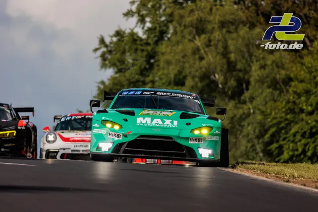 Aston Martin Vantage GT3 in türkis mit gelben Scheinwerfern führt eine Gruppe von GT3-Fahrzeugen durch eine Kurve auf dem Nürburgring.