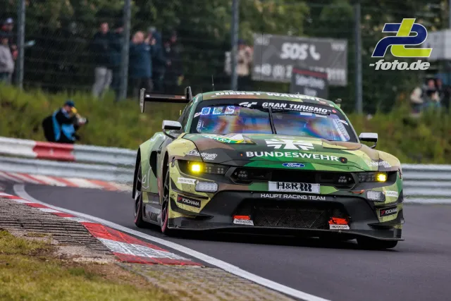 Ford Mustang GT mit Bundeswehr-Lackierung des Haupt Racing Team auf der Nordschleife mit eingeschalteten Scheinwerfern.