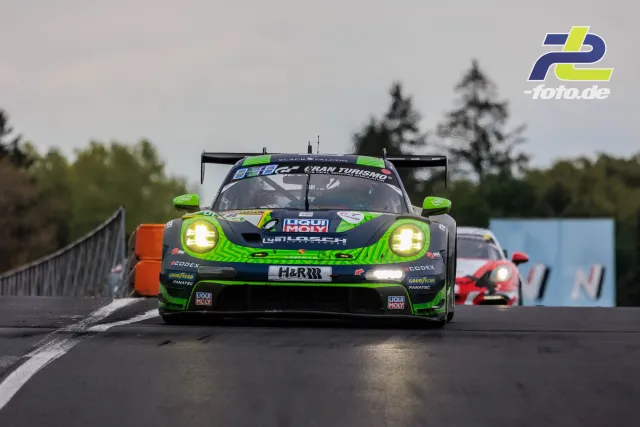 Porsche 911 GT3 R in grün-grauer Lackierung mit leuchtenden Scheinwerfern während des 24h-Rennens auf der Nordschleife.