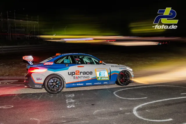 BMW M4 GT3 von up2race Santino bei Nacht auf der Nordschleife, im Hintergrund verschwommene Rennwagen durch Langzeitbelichtung.