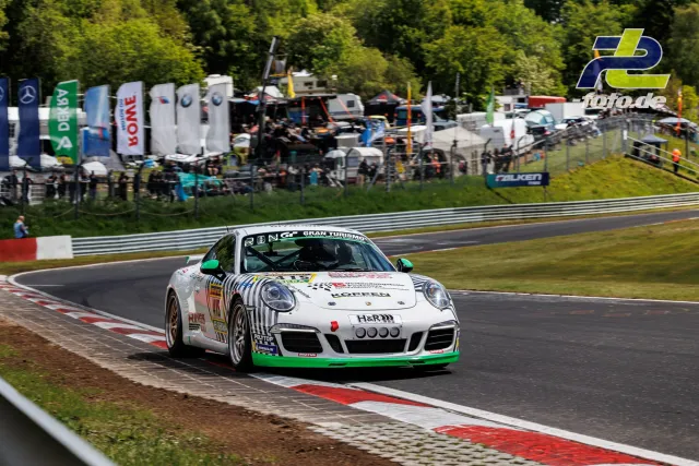 Weißer Porsche 911 mit grünem Dekor und Zebra-Streifen-Lackierung in einer Kurve auf der Nürburgring-Nordschleife während des Qualifyings.