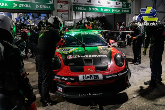 Porsche 911 GT3 R Nummer 900 beim Boxenstopp in der Nacht, umgeben von Mechanikern in der DEKRA-Box beim 24h-Rennen Nürburgring.