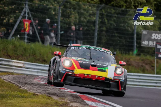 Porsche 911 GT3 R in schwarzer Lackierung mit rot-gelb-grünen Akzenten auf der Nordschleife beim 24h-Rennen am Nürburgring.