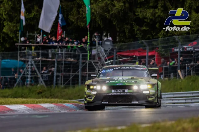Ford Mustang GT3 in olivgrüner Bundeswehr-Lackierung während des 24h-Rennens am Nürburgring, Tribüne im Hintergrund.