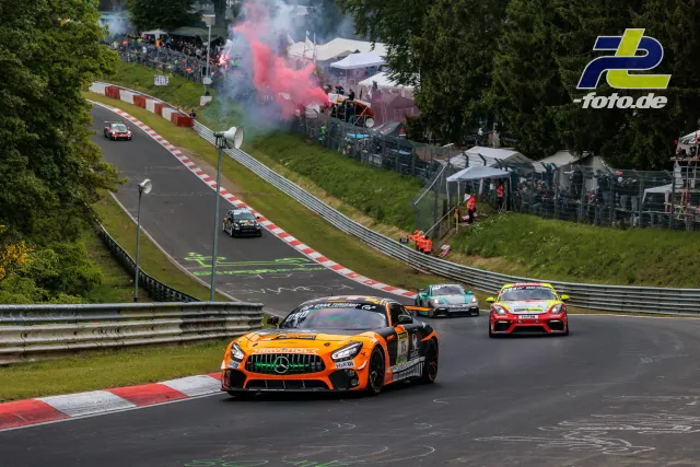 Mehrere Rennfahrzeuge auf der Nordschleife des Nürburgrings während der Formationsrunde mit Zuschauern und Raucheffekten im Hintergrund.