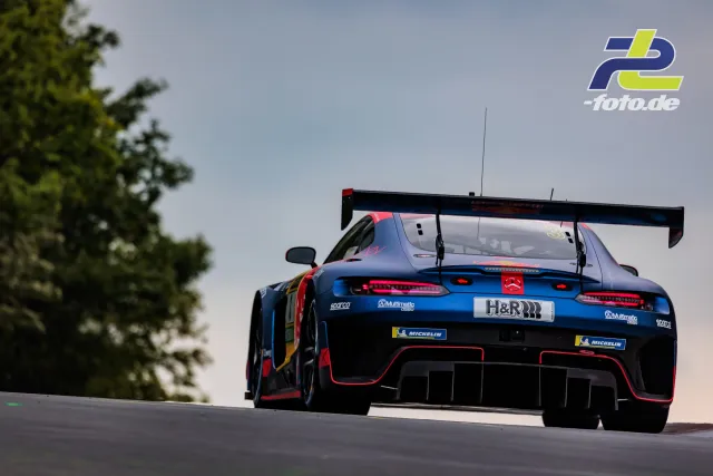 Mercedes-AMG GT3 in Blau mit roten Akzenten fährt über eine Kuppe auf der Nürburgring-Nordschleife, Heckansicht mit großem H&R-Schriftzug.