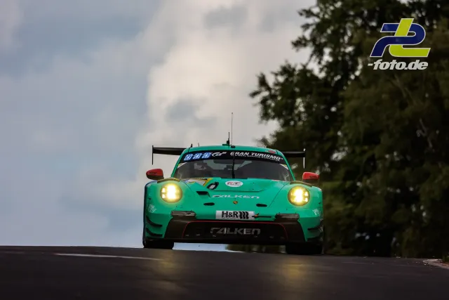 Porsche 911 GT3 R in türkiser Falken-Lackierung bei Dämmerung im 24h-Rennen auf dem Nürburgring mit eingeschalteten Scheinwerfern.