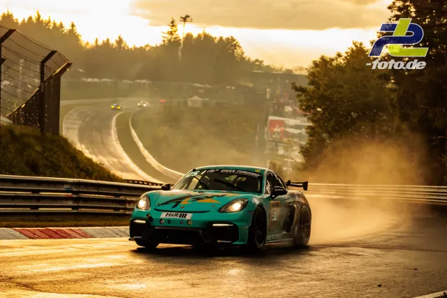 Porsche 718 Cayman GT4 #971 in türkisfarbener Lackierung auf der Nürburgring-Nordschleife bei Gegenlicht und Dunst während des Qualifyings.