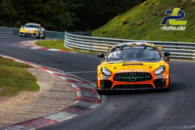 Orange-schwarzer Mercedes-AMG GT4 mit Gran Turismo-Banderole auf der Nordschleife, gefolgt von einem weißen Porsche.