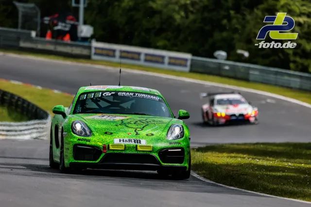 Grüner Porsche Cayman GT4 mit Spinnennetz-Design vor weißem Fahrzeug auf der Nordschleife beim 24h-Rennen Qualifying.