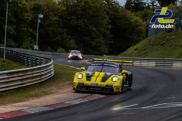 Porsche 911 GT3 R in gelb-schwarzer Lackierung auf der Nordschleife, gefolgt von einem zweiten Rennwagen während des 24h-Rennens.