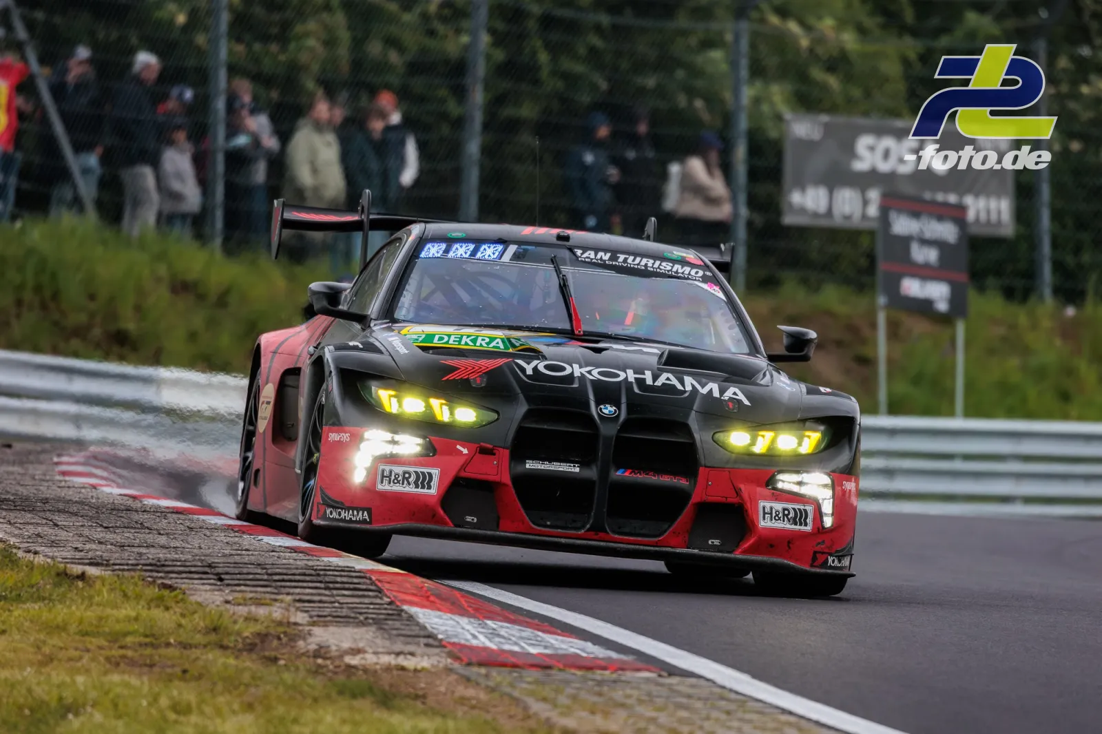 BMW M4 GT3 mit roter und schwarzer Lackierung im Regen auf der Nürburgring-Nordschleife während des 24-Stunden-Rennens.