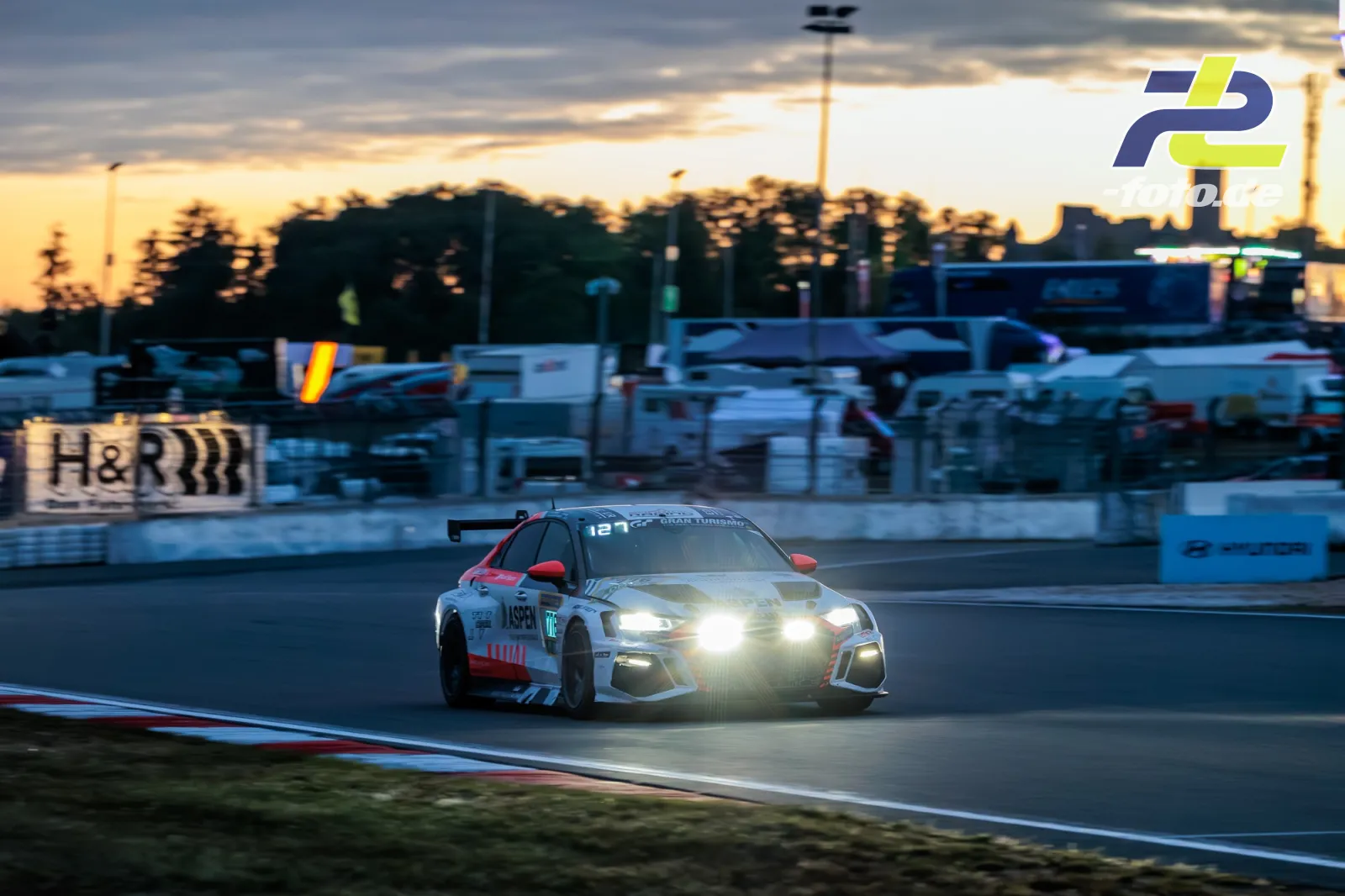 Audi R8 LMS GT3 bei Sonnenuntergang auf dem Nürburgring mit eingeschalteten Scheinwerfern während des 24h-Rennens.