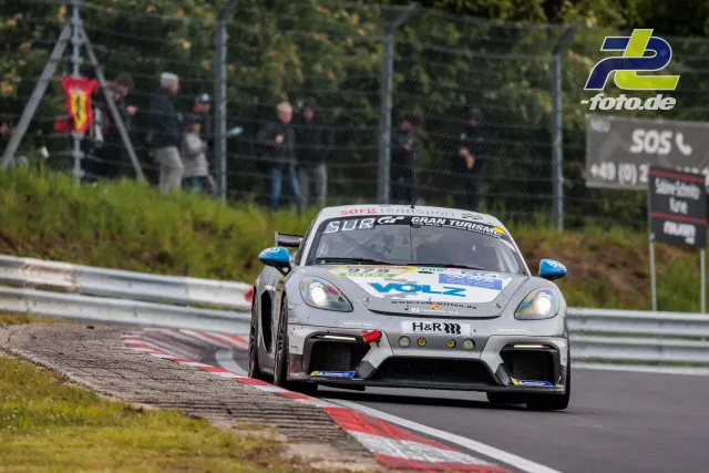 Weißer Porsche 718 Cayman GT4 mit Startnummer 979 über Randsteinen auf der Nürburgring-Nordschleife während des 24h-Rennens.