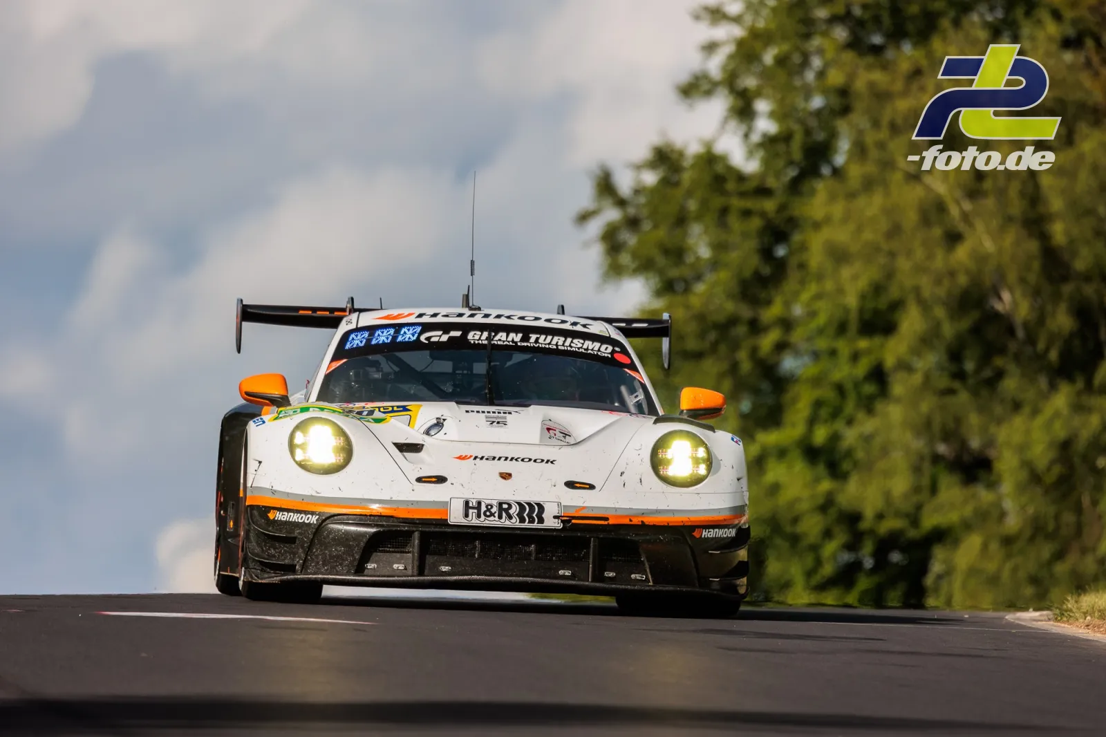 Porsche 911 GT3 R auf der Nürburgring-Nordschleife beim 24h-Rennen, frontale Ansicht über einer Kuppe mit Bäumen im Hintergrund.