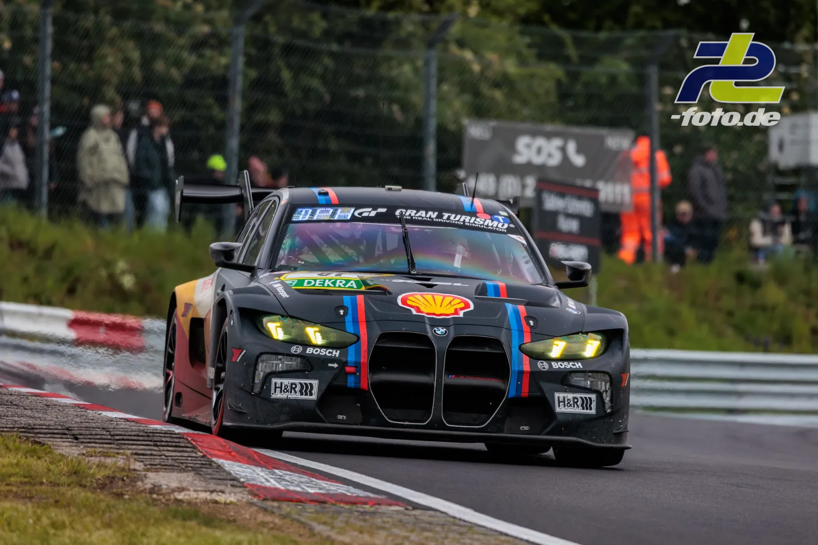 BMW M4 GT3 mit Shell-Sponsoring in Kurve auf der Nordschleife beim 24h-Rennen, Randstein und Zuschauer im Hintergrund