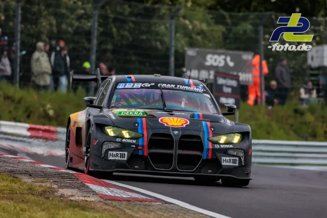 BMW M4 GT3 mit Shell-Sponsoring in Kurve auf der Nordschleife beim 24h-Rennen, Randstein und Zuschauer im Hintergrund
