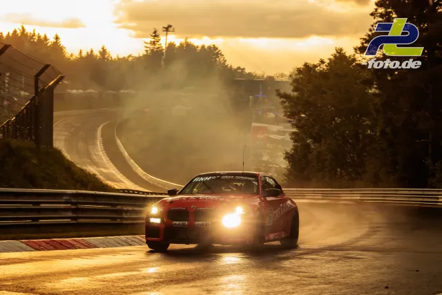 Rotes Fahrzeug in der Abendsonne auf der Nordschleife, dramatisches Gegenlicht und Dunst über der Strecke.
