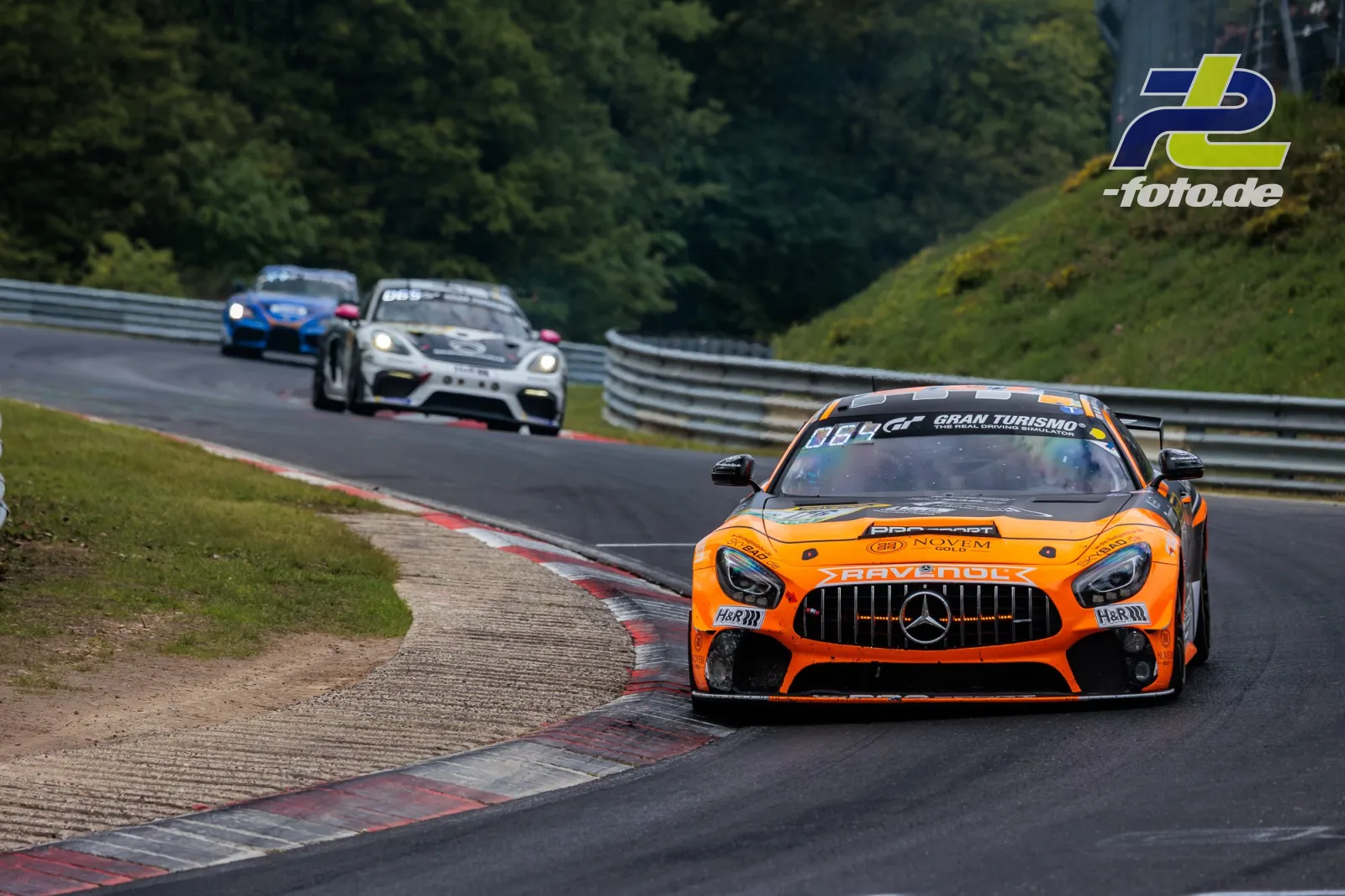 Mercedes-AMG GT4 in orange auf der Nordschleife beim 24h-Rennen am Nürburgring, gefolgt von weiteren Fahrzeugen in Kurvenausfahrt.