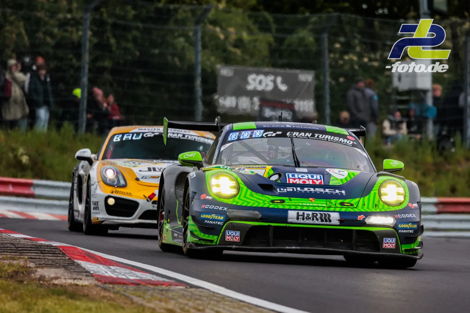 Zwei Porsche 911 GT3 R im Rennen auf der Nordschleife beim 24h-Rennen, vorne grün-schwarzer Wagen mit Heckflügel, dahinter weiß-oranges Fahrzeug.