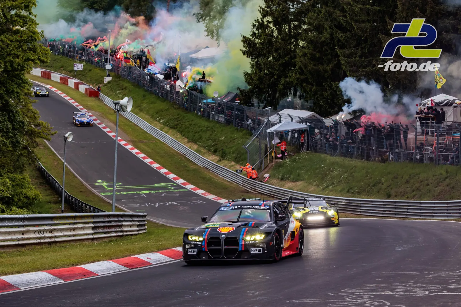 BMW M3 Touring 24h (#81) während der Formationsrunde auf der Nordschleife, Zuschauer mit farbigen Rauchfackeln im Hintergrund, 24h Nürburgring 2026