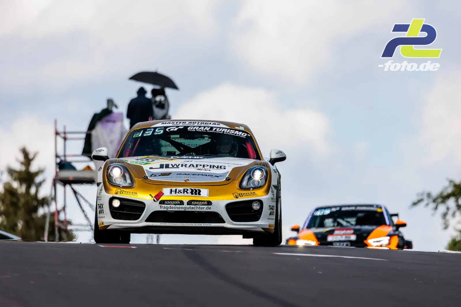 Porsche Cayman CM12 #455 des Teams RSG SH e.V. auf einer Kuppe der Nordschleife beim 24h-Rennen am Nürburgring unter bewölktem Himmel.