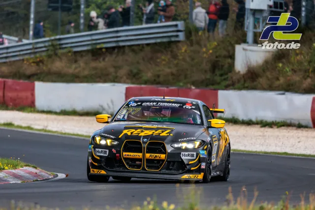 BMW M4 GT4 #177 in schwarz-gelber RËBEL-Lackierung in einer Kurve auf dem Nürburgring mit Zuschauern im Hintergrund.