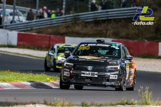 Schwarzer Opel Corsa Nummer 380 mit orangen Akzenten auf der Nordschleife, gefolgt von einem weiteren Fahrzeug.