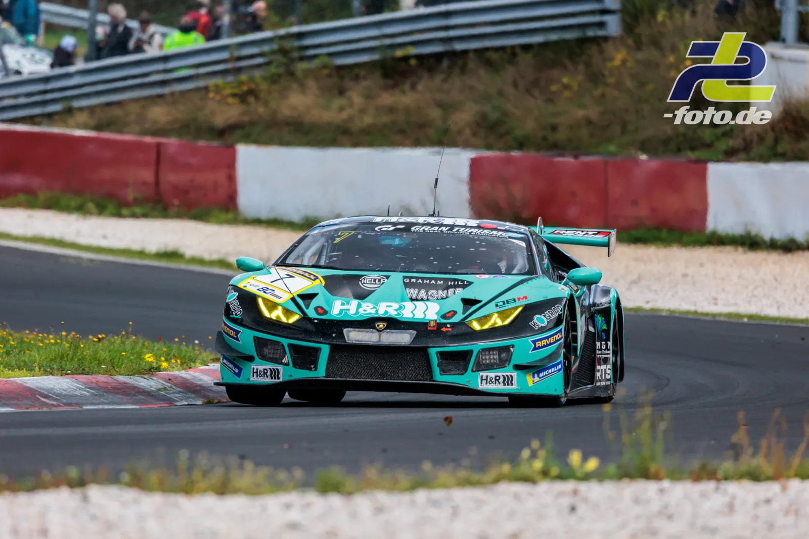 Türkis-grüner Lamborghini Huracán GT3 in Kurve auf der Nordschleife, Zuschauer an Leitplanke im Hintergrund, NLS Rennen.