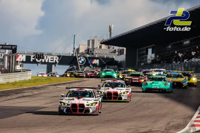 Zwei BMW M4 GT3 führen das Feld durch eine Rechtskurve auf dem Nürburgring, im Hintergrund die Haupttribüne.