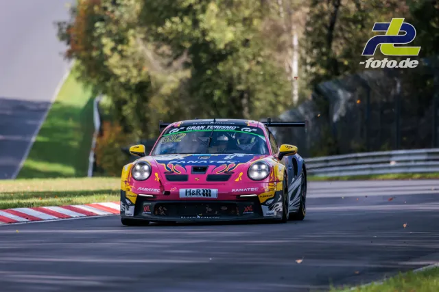 Porsche 911 GT3 R in pink-gelber Lackierung auf der Nordschleife, Frontansicht während des Rennens am Nürburgring.