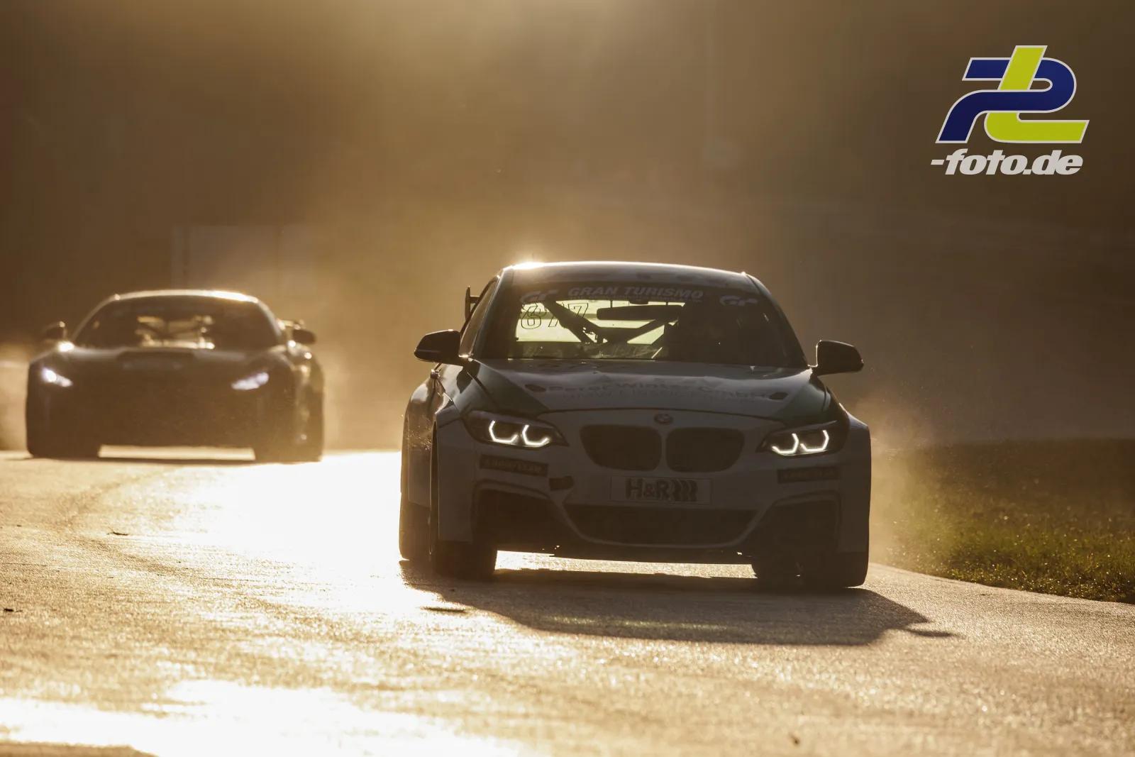 BMW M240i Racing Cup im Gegenlicht auf der Rennstrecke, gefolgt von einem weiteren Fahrzeug in staubiger Atmosphäre beim NLS-Qualifying.