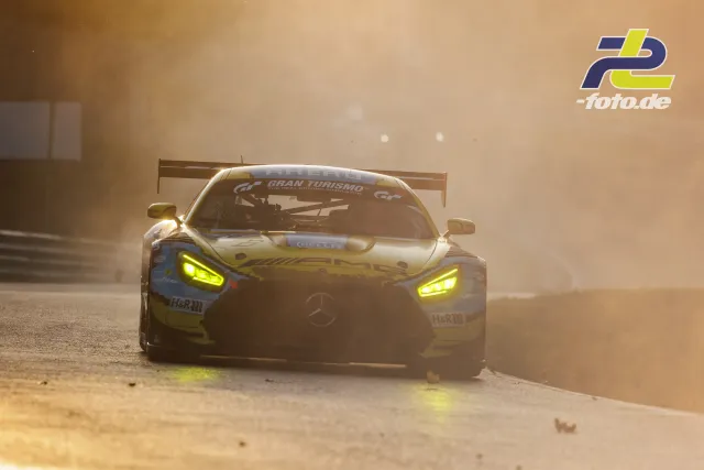 Mercedes-AMG GT3 mit gelben Scheinwerfern auf der Nordschleife im Gegenlicht, aufgewirbelter Staub sorgt für dramatische Stimmung.