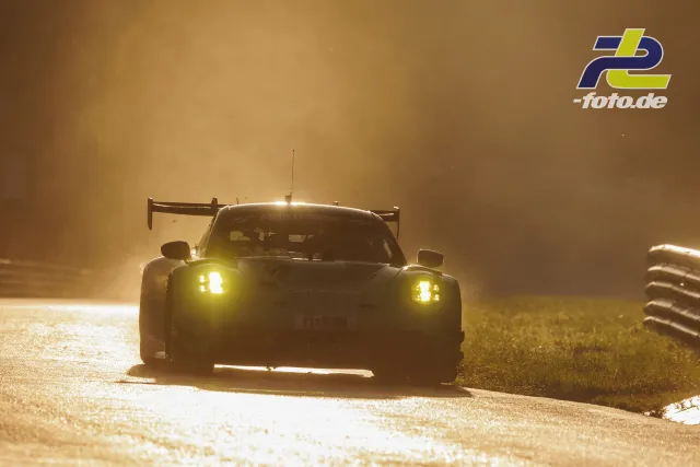 Rennwagen im Gegenlicht bei staubiger Atmosphäre auf dem Nürburgring, gelbe Scheinwerfer leuchten durch den Dunst.